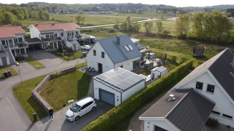 Solpaneler monterade på ett fristående garage med platt tak intill en vit villa.