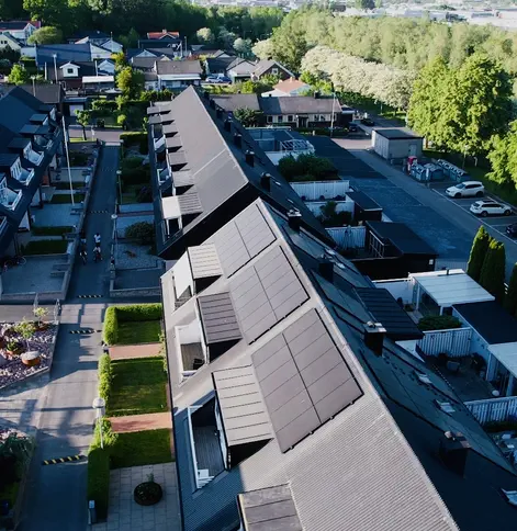 Drönarbild på integrerade svarta solpaneler på taket av ett modernt radhusområde.