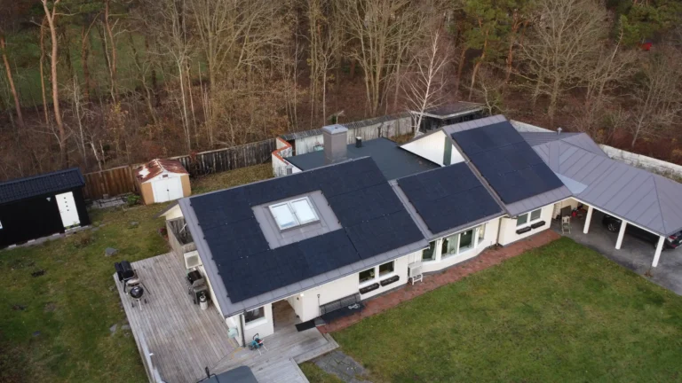 Integrerade svarta solceller på ett grått plåttak på en ljus enplansvilla.