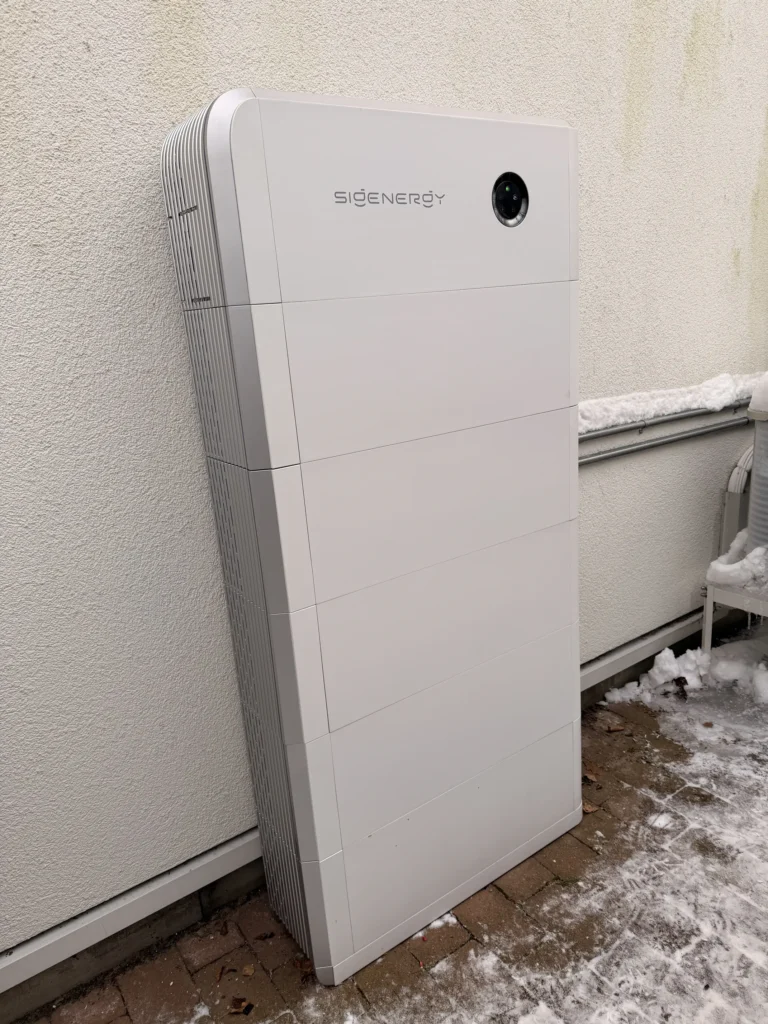 Ett vitt Sigenergy solcellsbatteri installerat utomhus mot en fasad i vintermiljö.