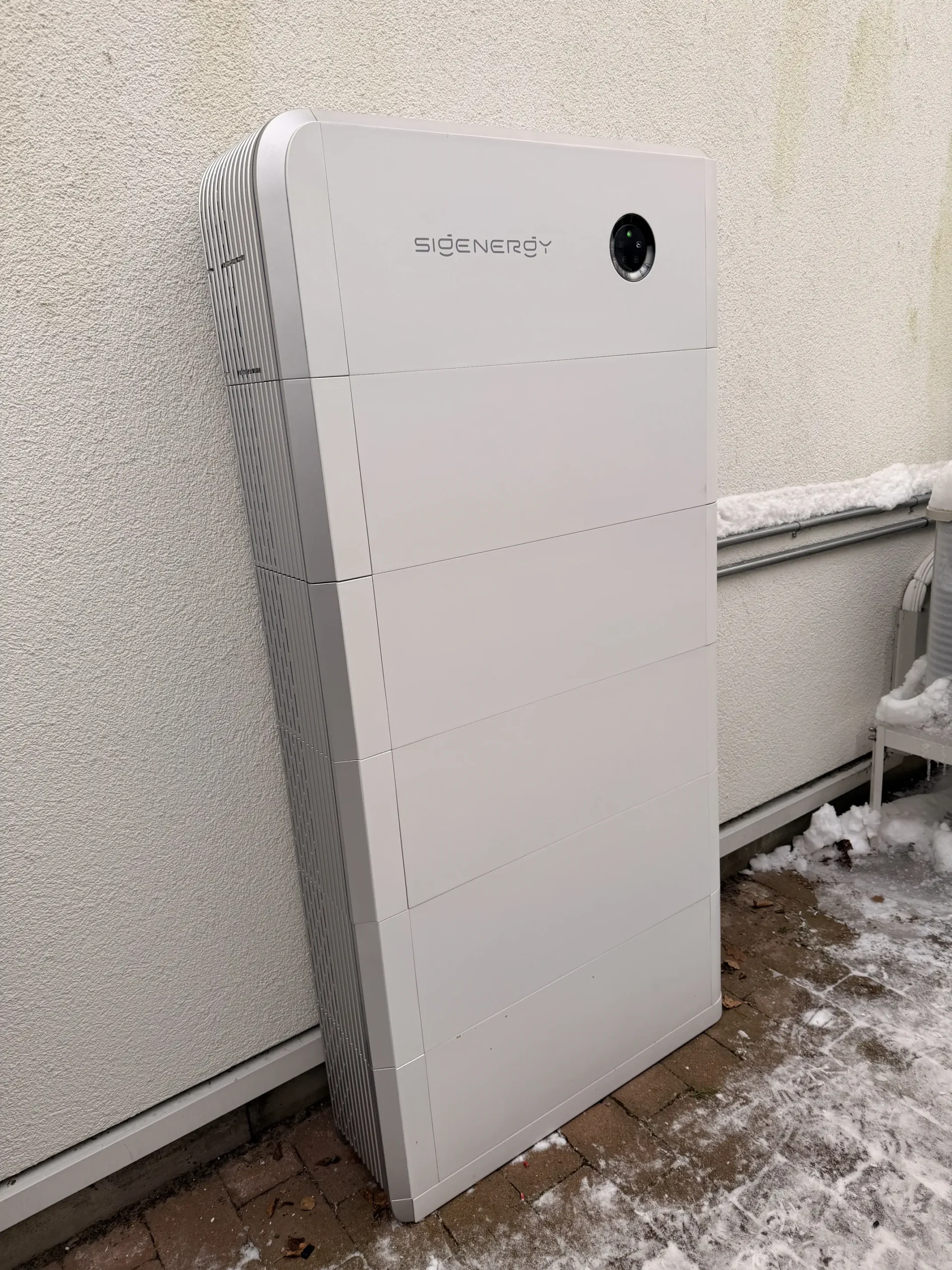 Ett vitt Sigenergy solcellsbatteri installerat utomhus mot en fasad i vintermiljö.