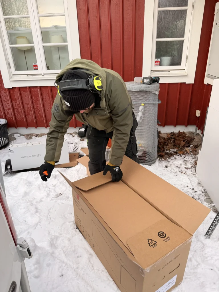 Installatör i vinterarbetskläder packar upp ett Sigenergy batterisystem utomhus