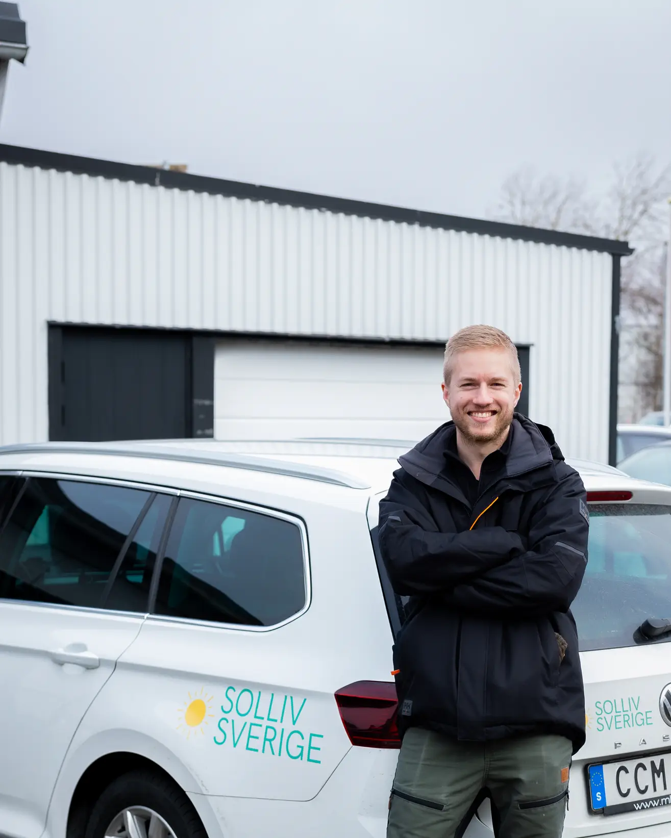 Leende Simon Myrving från Solliv Sverige med armarna i kors framför en vit företagsbil.